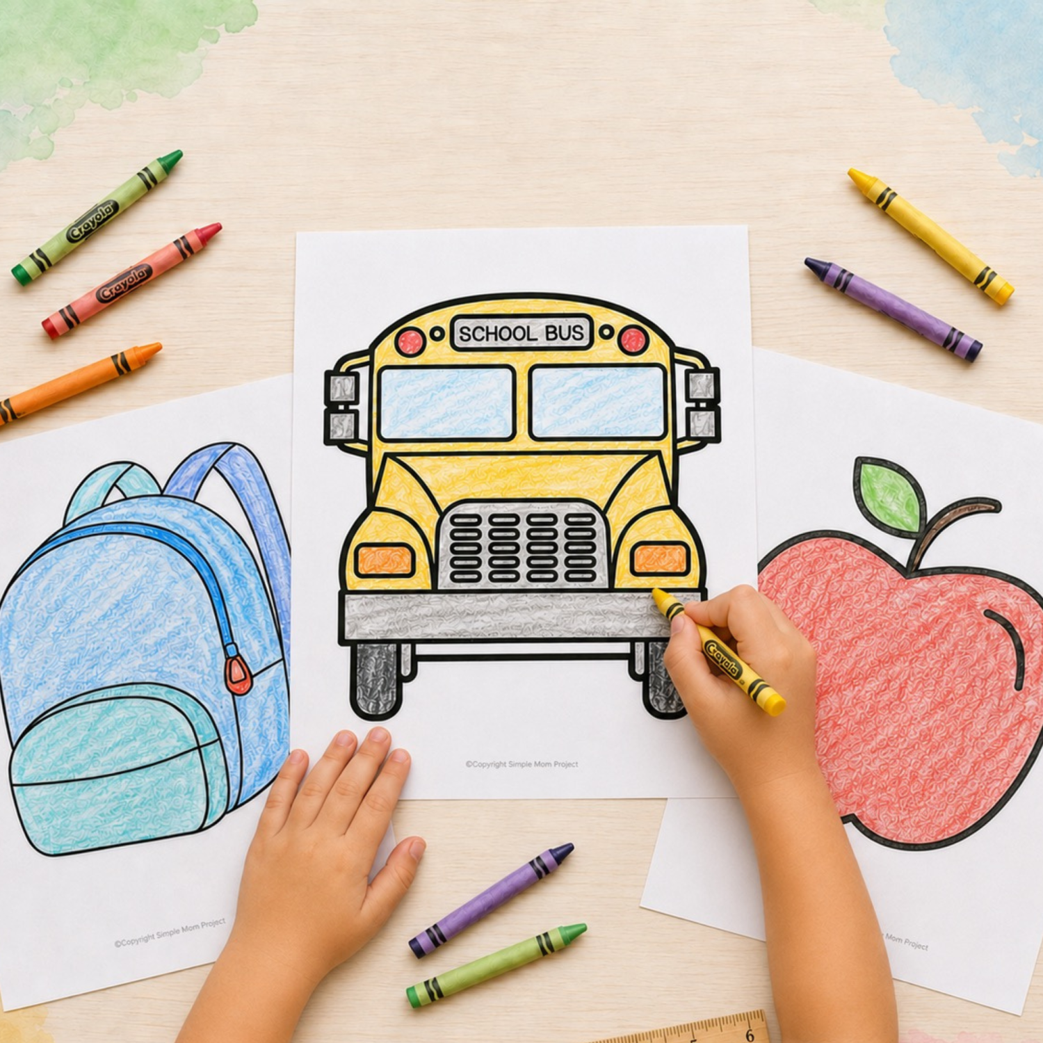 Child coloring a yellow school bus template with completed backpack and apple coloring pages on a classroom table.